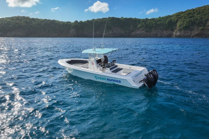 Boat named Ocean Runner on blue sea near wooded coastline.