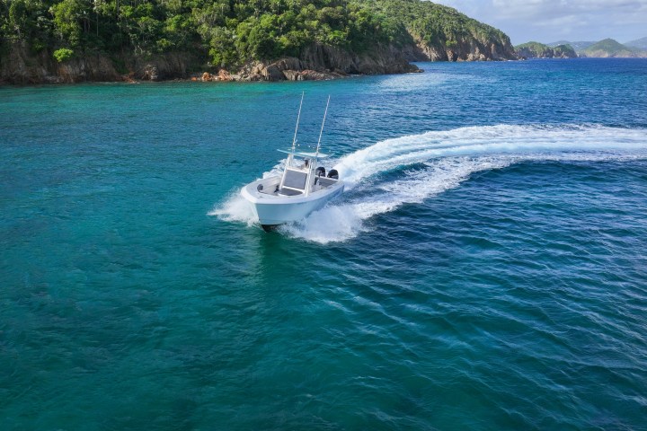 A speedboat making a turn on clear turquoise water near a lush, green coastal landscape.