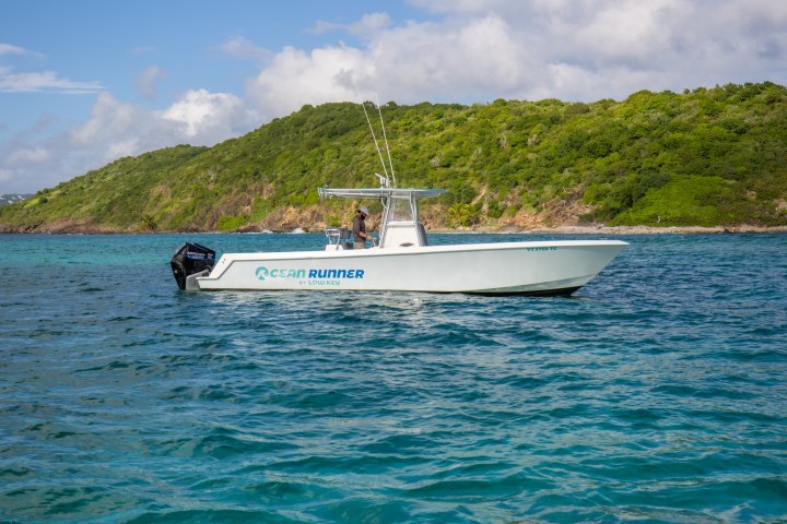 Boat on turquoise water with green hills and blue sky in the background.
