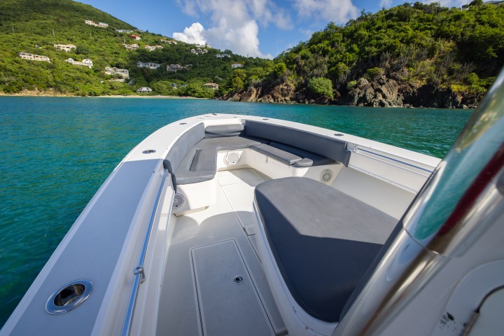 View from boat's deck towards green hills and turquoise water.