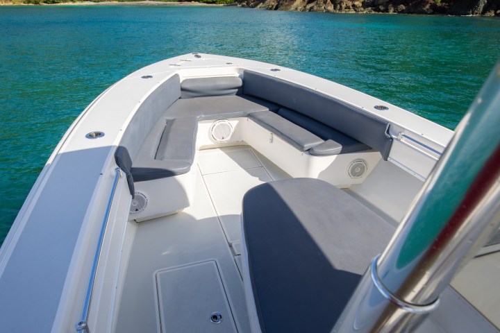 Boat deck with seats, overlooking turquoise water and green hillside with houses.