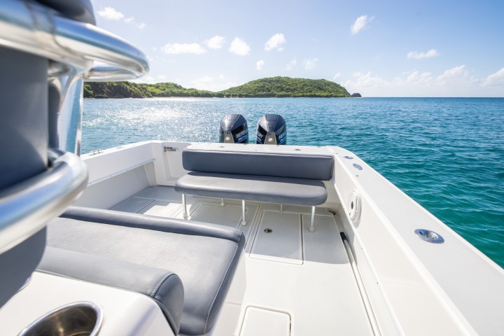 Boat deck with seats and railing, overlooking ocean and green island under clear sky.