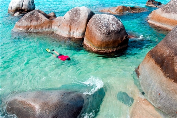 This girl is walking through the boulders at the Baths in Virgin Gorda in the sunlight and through the aqua water