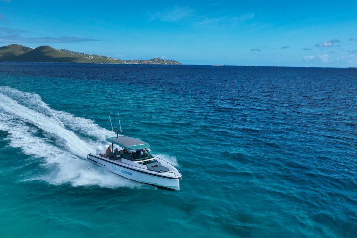 Boat speeding on clear blue ocean with distant islands under a bright blue sky.