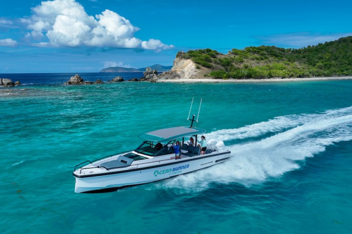 A motorboat speeds across turquoise waters near a lush island under a blue sky with clouds.