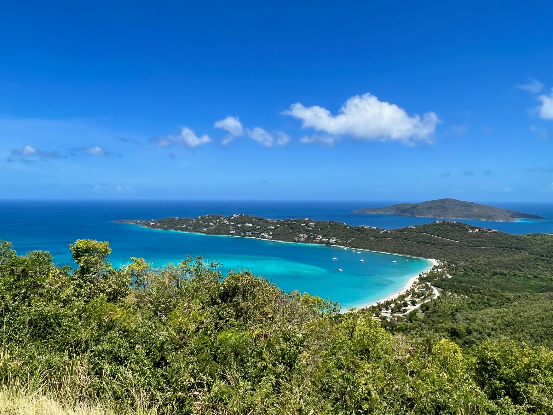 a view of a beach next to a body of water with Magens Bay in the background