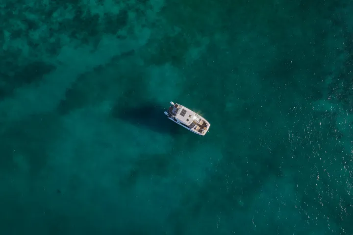 Aerial view of a lone white yacht on clear turquoise water.