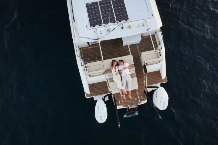Couple relaxing on a yacht's deck over calm water, viewed from above.
