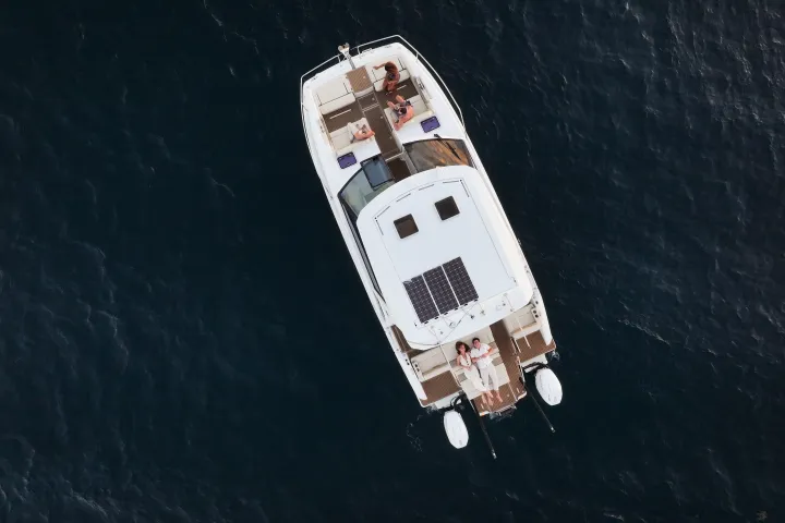 Aerial view of a boat with people sunbathing on deck, surrounded by dark blue water.