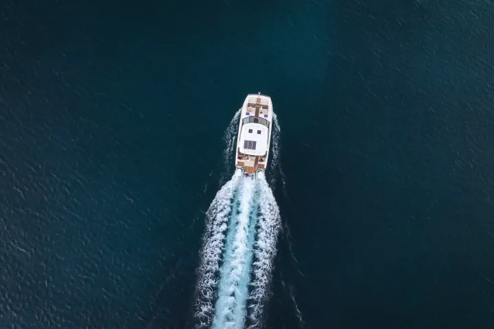 Aerial view of a boat moving through the dark blue ocean, leaving a trail of white wake behind.