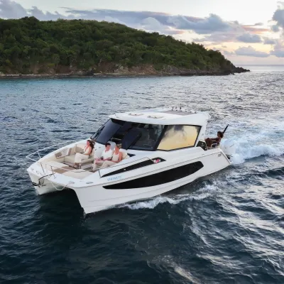 A motorboat with people cruising near a forested island at sunset.