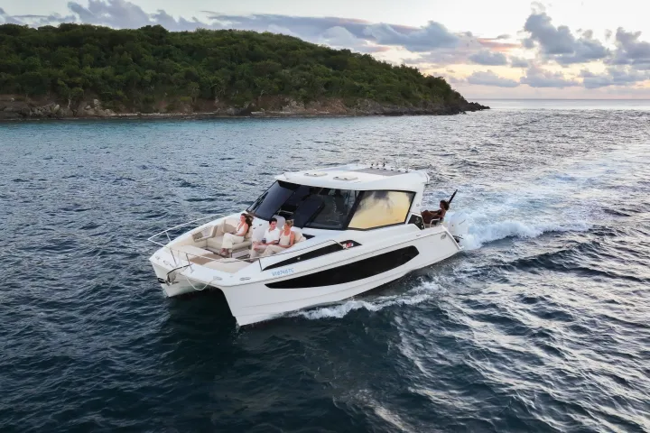 A motorboat with people cruising near a forested island at sunset.