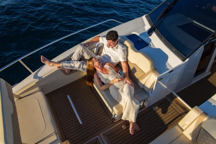Couple relaxing on a boat's deck, on cushioned seats, with ocean in the background.