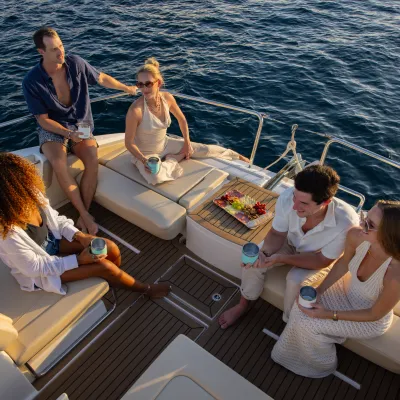 Group of people relaxing and talking on a boat with drinks and a platter of food.