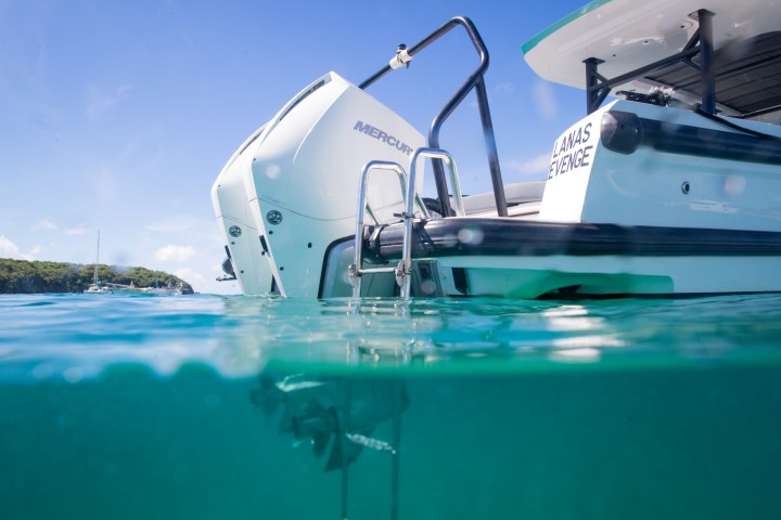 Boat stern with visible outboard motor and ladder, half-submerged in clear water.