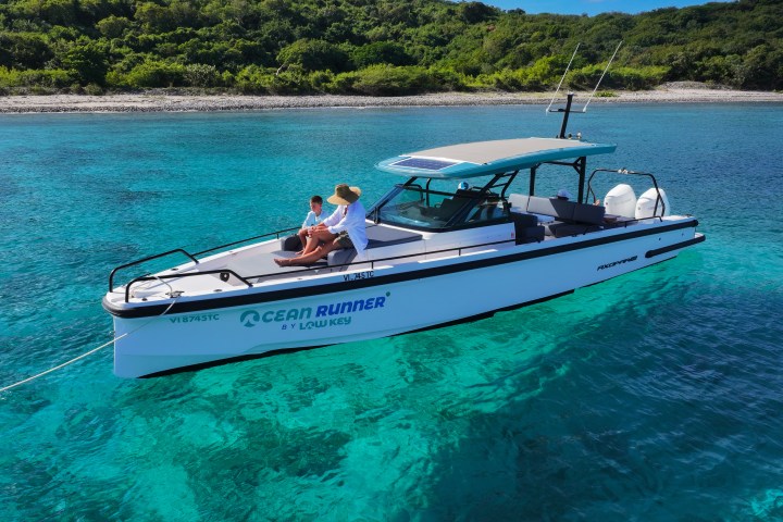 Boat on clear turquoise water near a lush green island shore.