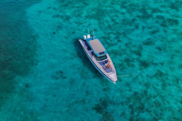 Aerial view of a boat on clear turquoise water with two people on board.
