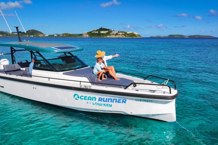 Boat named Ocean Runner in clear blue water with people relaxing, tropical islands in the background.