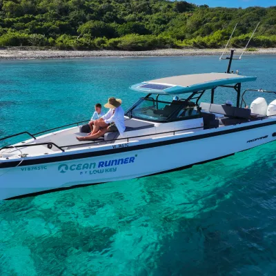 A white motorboat with people onboard floats on clear turquoise water near a green shoreline.