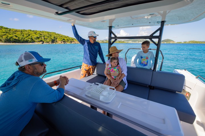 Family on a boat enjoying a sunny day near an island with turquoise water.