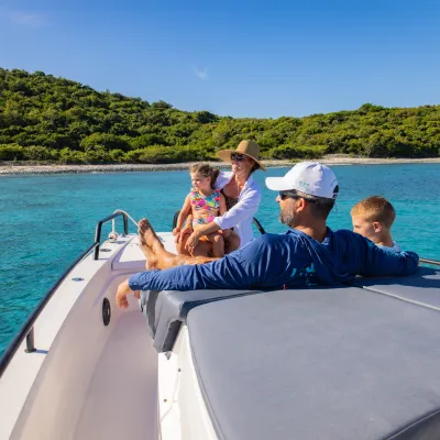 Family on a boat enjoying a sunny day near a lush green island.