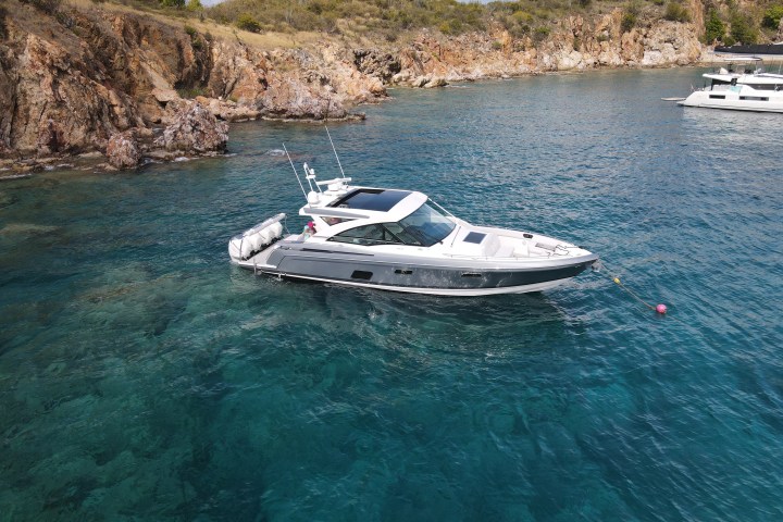Motorboat anchored near rocky shoreline in clear blue water.