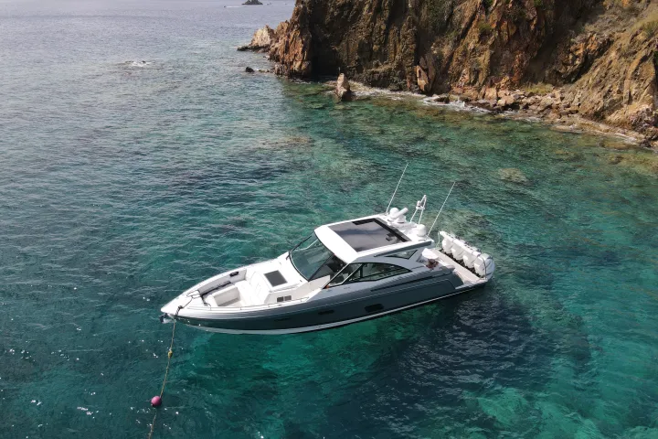White boat anchored near rocky coastline in clear blue-green water.