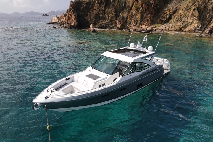 A yacht anchored near a rocky coastline in clear blue water.