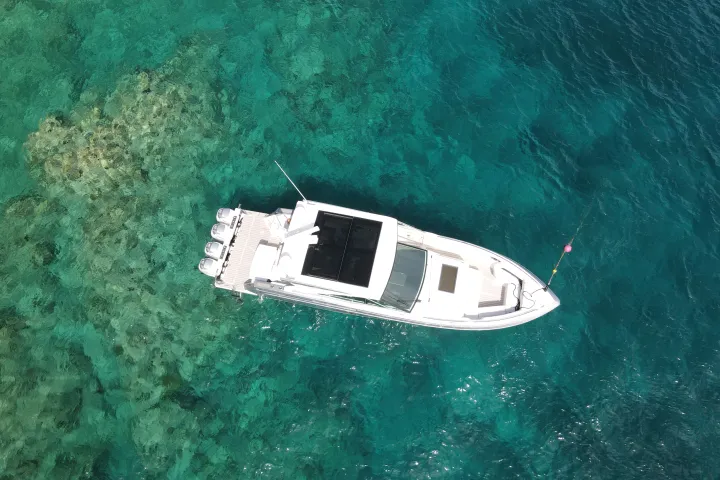 Aerial view of a white yacht on clear turquoise water.