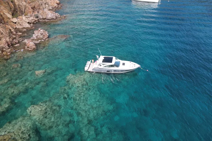 Boat on clear blue water near rocky shoreline, other boats in background.