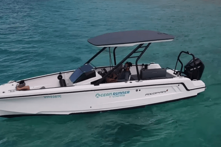 White motorboat on clear turquoise water with two people onboard.