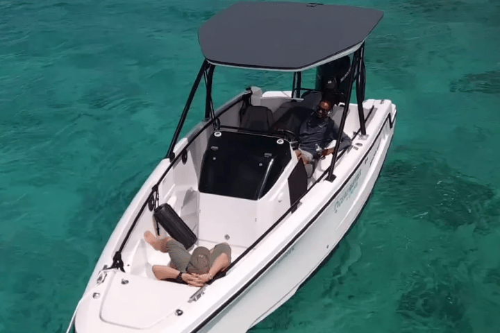 Two people relax on a small motorboat in clear turquoise water.